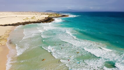 Aerial view of a crowd of surfers enjoying the waves on the beach of Corralejo, Fuerteventura Island, Spain.