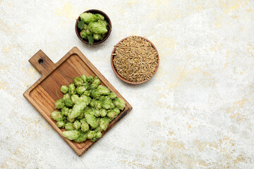 Board with green hops cones and bowl of seeds on white grunge background