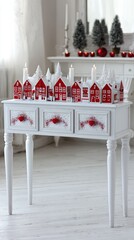 A charming display of red houses and snowy Christmas trees arranged on a white console table, creating a festive and cozy holiday scene.