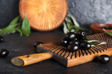 Wooden board with tasty black olives and leaves on black background