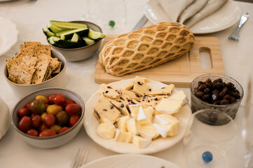 A festive table spread with cheese, bread in puff pastry, crackers, cucumbers, olives, and cherry tomatoes, ready for a family celebration.