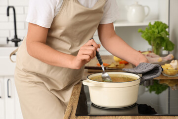 Young housewife cooking soup on stove in kitchen, closeup