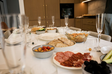 Elegant dining table with charcuterie, bread, vegetables, olives, and appetizers prepared for festive family meal or celebration in modern home kitchen.