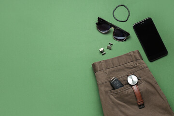 Stylish men's accessories with trousers and modern mobile phone on green background