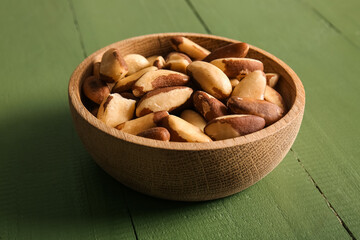 Bowl with tasty Brazil nuts on green wooden background