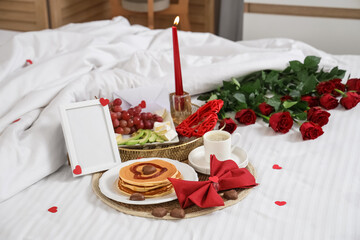 Tasty breakfast with blank frame on bed in room decorated for Valentine's Day