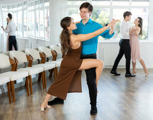 Expressive guy in blue shirt and black trousers rehearsing elegant tango with young female partner...