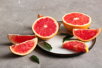 Plate with cut fresh grapefruits and leaves on grey background