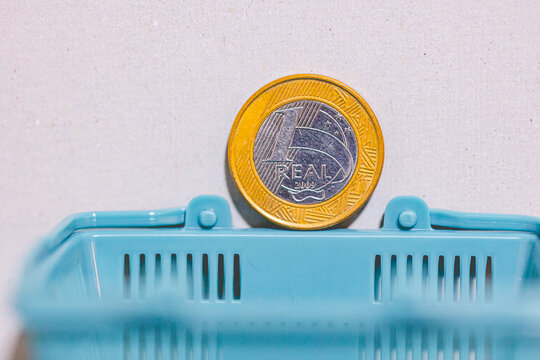 1 Real, Real Brasileiro, Dinheiro, Brasil, Moeda brasileira. Uma moeda de 1 Real sobre uma miniatura de cesta de mercado. Foto sobre infla&ccedil;&atilde;o e crise financeira no Brasil. 