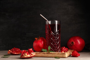Glass of fresh pomegranate juice and fruits on white table near black wall