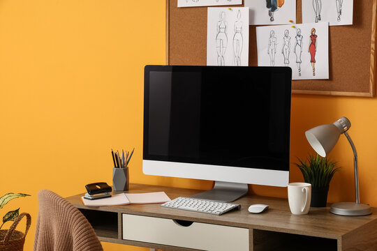 Modern workplace of fashion designer with computer and sketches near yellow wall in room