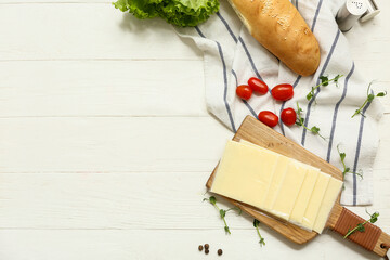 Board with slices of delicious processed cheese, fresh vegetables and bread on white wooden table