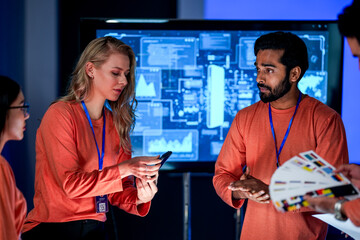 A data analytics team in a command center reviews a live security feed on a mobile device. They are collaborating on a strategy to respond to a new threat on the network.