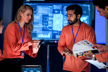A data analytics team in a command center reviews a live security feed on a mobile device. They are collaborating on a strategy to respond to a new threat on the network.