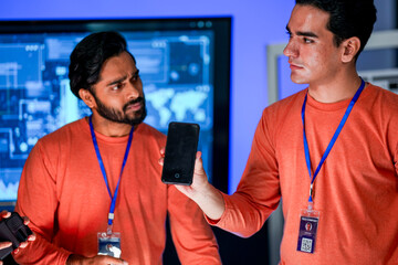 A data analytics team in a command center cross references information from a mobile device with a printed report, while a global data dashboard is displayed on a large screen.