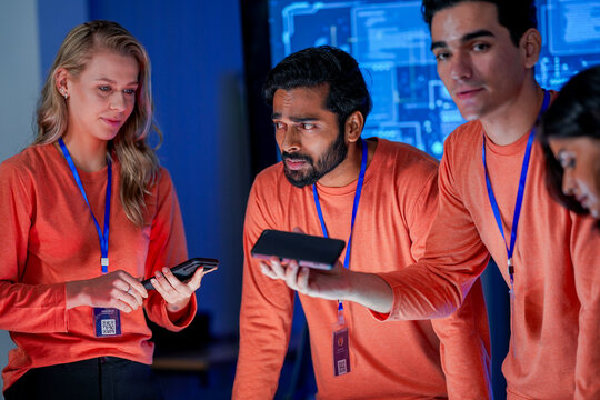 A data analytics team in a command center reviews a live security feed on a mobile device. They are collaborating on a strategy to respond to a new threat on the network.