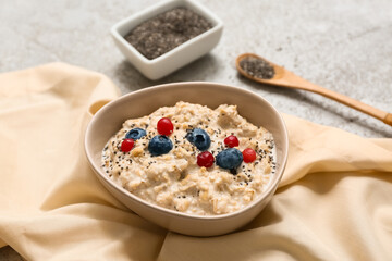 Bowl with tasty oatmeal, berries and chia seeds on grey grunge background