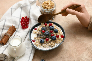 Female hand with tasty oatmeal, berries and chia seeds in bowl on beige grunge background
