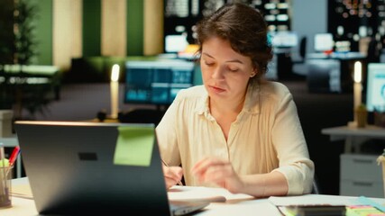 Corporate employee focused on writing a detailed report under a desk lamp. Summarizing updates, organizing the agenda and drafting insights for the corporation management plans. Camera B. - Powered by Adobe