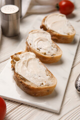 Board of tasty bruschetta with processed cheese on white wooden background