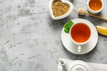 Cup of hot buckwheat tea with mint leaves, lemon slice and dipper on grey grunge background