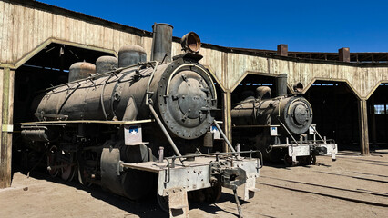 An old steam locomotive stands parked on a siding near a dock, covered in dust and signs of long...