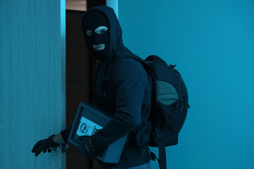 Male thief with stolen safe at door in dark room