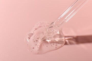 Dripping cosmetic product from pipette on pink background, closeup