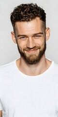 Handsome man with curly hair and a beard poses confidently in a white shirt against a plain background.