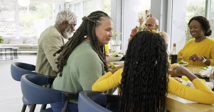 Multigenerational family passing salad and hugging child before sharing bread rolls in dining room