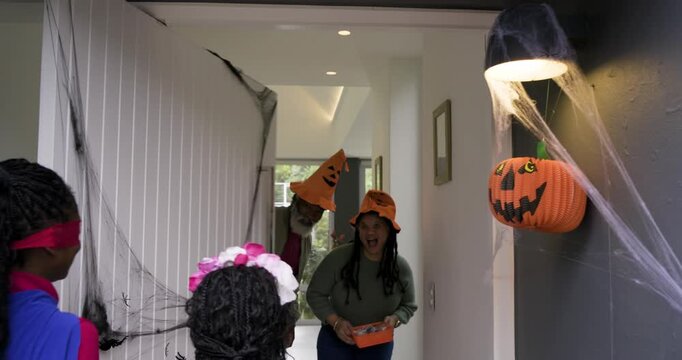 Two African American girls holding buckets knocking on door and receiving candy, copy space