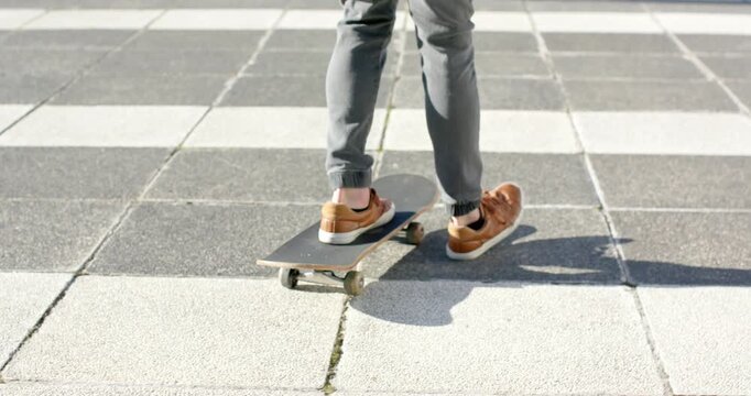 Shifting weight pushing left foot propelling male skateboarder riding board across sunlit plaza
