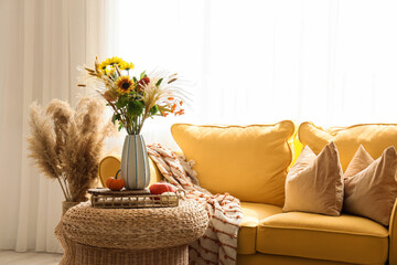 Vase with autumn flowers and pumpkins on table in living room interior