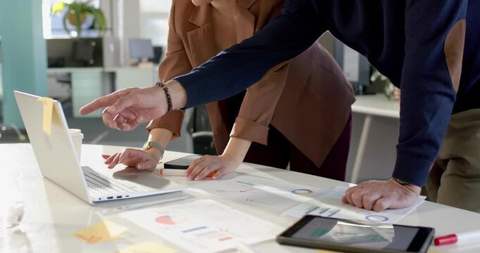 Prompted by data diverse coworkers pointing charts tapping laptop, explaining trends in open office