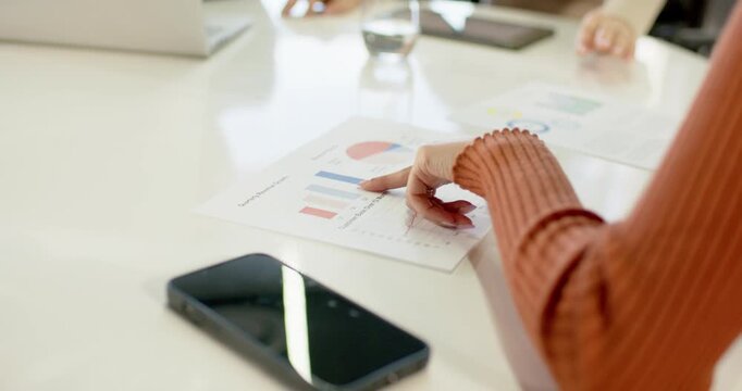 Data chart driving Diverse coworkers highlighting graphs tapping tablet reviewing laptop at table