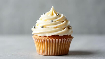 A delicious vanilla cupcake being decorated with silver sprinkles in a bakery studio, perfect for a birthday party or sweet treat promotion