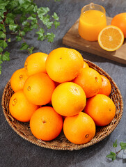 Fresh Sweet Navel Oranges in Wicker Basket with Orange Juice and Herbs on Dark Stone Kitchen Counter