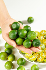 Fresh Small Green Limes and Orange Hainan Kumquats in Hands - Citrus Fruit Collection