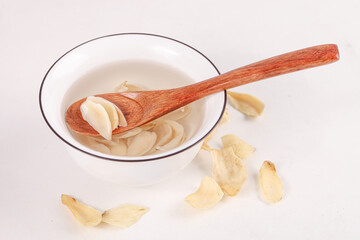 Dried Garlic Cloves in White Bowl with Wooden Spoon on White Background