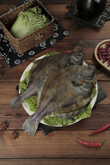 Fresh Whole Flounder Fish on Plate with Lettuce Garnish and Cooking Ingredients on Rustic Wood Table