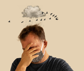 Adult male wearing a mask with head down and hand on forehead, surreal rain cloud and birds above