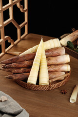 Fresh bamboo shoots in wicker basket with Asian cooking ingredients on wooden table