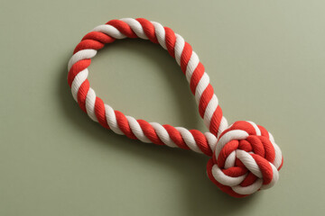 Red and white twisted thick rope forming loop with knot on light green surface, concept of strength, unity, support, teamwork, problem solving, secure connection