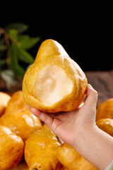 Fresh Cut Pear Half Held in Hand with Whole Pears on Wooden Table