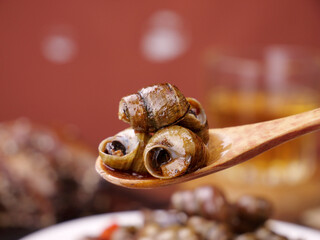 Stir-Fried Whelk Sea Snails with Spicy Red Sauce on Wooden Spoon - Traditional Seafood Delicacy