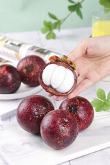 Fresh Thai Mangosteen Fruit with White Flesh Segments in Hand on White Wood Background