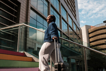 Businesswoman walking up colorful stairs with rolling luggage in urban setting
