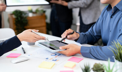 A close-up view of two business professionals collaborating and discussing data on a tablet. Their...