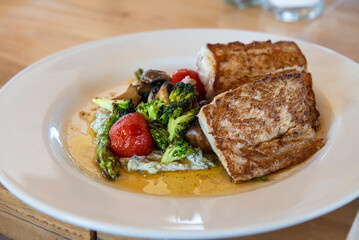 Buttered fish with vegetables cooked in butter, on a white plate on a wooden table in a restaurant