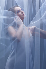Portrait of a young female covered with veil. Woman is dressed in a peignoir and wears a necklace and earrings.